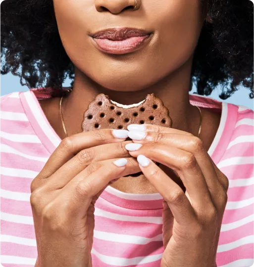 A closeup of a woman taking a bite of a Skinny Cow ice cream sandwich. 